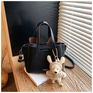 Detail of black pebbled leather tote with detachable strap and cute brown teddy bear charm