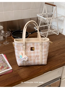 Detail of pink plaid bucket bag with cartoon prints and a plush bunny charm on a table