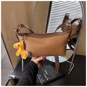 Détail du sac bandoulière en cuir caramel avec pendentif cheval jaune et bords bruns