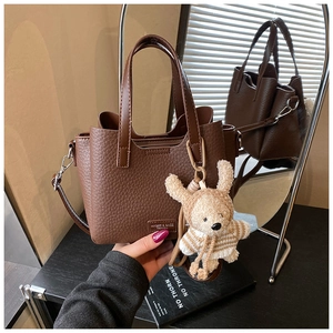 Close-up of brown litchi pattern PU leather handbag with a cute plush bear charm detail