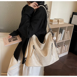 Detailed close-up of large beige hobo bag with baseball charm and textured finish