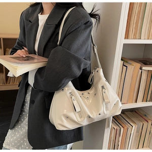Close-up of off-white hobo bag with silver studs and decorative zippers in a lifestyle setting
