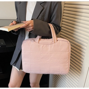 Detailed view of pink quilted laptop bag with cylindrical handles held by a model