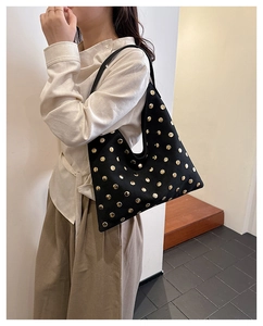 Model wearing a black hobo tote bag with gold rivets in a minimalist interior setting