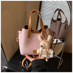 Detail view of pink lychee grain leather tote with brown handles and plush bear charm