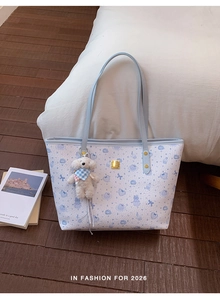 Détail d'un sac cabas bleu clair avec motifs animaux, logo métal et breloque ours