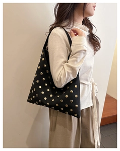 Detailed side view of black canvas tote bag with golden rivets worn as a shoulder bag