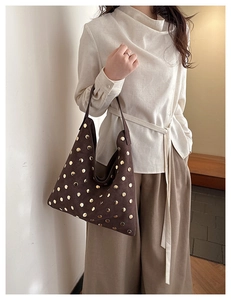 Detail of brown suede tote bag with golden rivets styled with a minimalist beige outfit