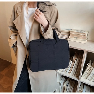 Detail of a black quilted laptop bag with a padded handle in a cozy home office setting