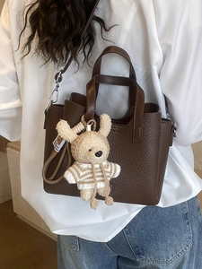 Minimalist brown pebbled leather tote bag with a plush bunny charm on a casual model