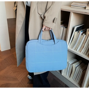 Detail of light blue quilted laptop bag with grid pattern and handles in library setting