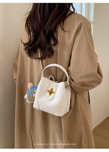 Sac seau minimaliste en cuir blanc avec fermoir doré porté par un mannequin femme
