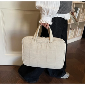 Close-up of a beige quilted laptop sleeve with soft fabric texture and padded handles