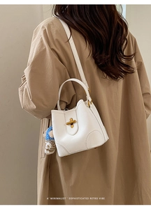 Détail du sac seau blanc minimaliste avec fermoir doré et breloque poupée tricotée