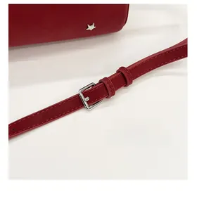 Détail d'un sac en cuir rouge montrant la bandoulière réglable et les rivets en étoile