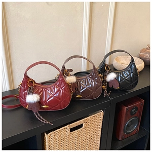 Detailed view of quilted half-moon handbags in red, brown, and black with pom-pom charms