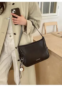 Detail of dark brown leather handbag with contrast stitching and baseball charm accessory