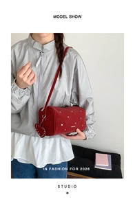 Vue détaillée du sac cylindrique rouge avec clous en étoile et pendentif en forme de cœur