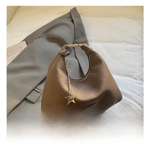 Dettaglio borsa hobo in pelle caffè con ciondolo a stella dorata su blazer grigio