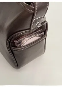 Detail view of dark brown leather side pocket with white stitching on minimalist handbag