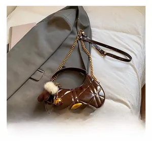 Detail of brown quilted faux leather handbag with gold chain and white pompom charm