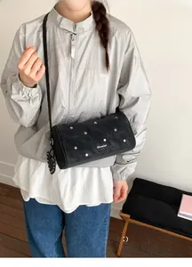 Détail du sac bandoulière cylindrique noir avec clous en étoile et pendentif en cœur