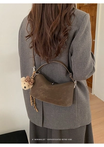 Close-up of a dark brown suede underarm bag with a cute bear charm on a grey wool coat