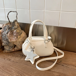 White leather bowling bag with star pendant on a dark wooden surface with shoulder strap