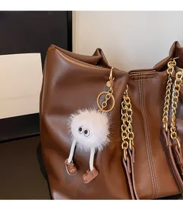 Close-up of a white plush monster charm with long legs on a brown leather tote bag