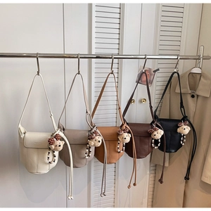 Detail of five leather shoulder bags with teddy bear charms on a minimalist display