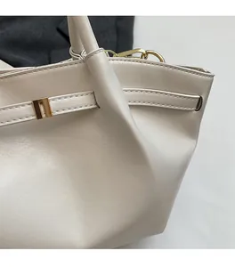 Détail de la texture en cuir fin et boucle dorée sur un sac fourre-tout crème