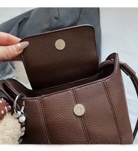 Detail of brown leather bucket bag showing dual magnetic buckles and silver hardware accents