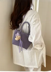 Detail of purple matte leather bucket bag featuring a plush bear charm and tassel
