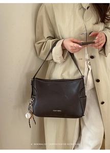 Detailed view of deep chocolate leather shoulder bag featuring a silver logo and baseball charm