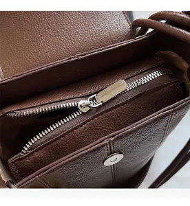 Detail view of smooth silver zipper and magnetic snap closure on brown leather bag