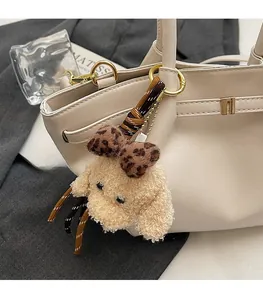 Détail d'un charme de sac chiot en peluche kaki avec nœud léopard et anneau doré