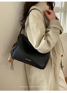 Detail of a retro black leather shoulder bag with a heart-shaped brown charm and metal logo