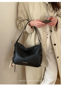 Detail of vintage black leather shoulder bag with white stitching and baseball charm