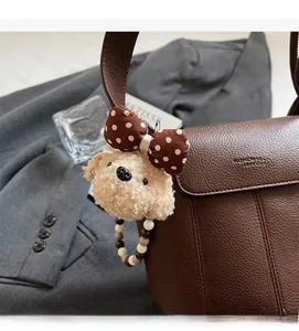 Close-up of a plush puppy charm with polka dot bow on a brown leather bucket bag