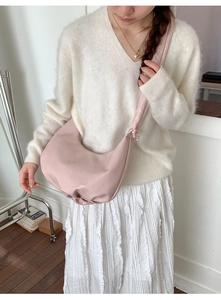 Detail of a pink pleated crescent shoulder bag shown on model in a minimalist room