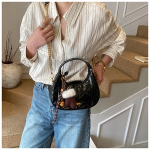 Close-up of black quilted leather crescent bag with gold chain and decorative charms