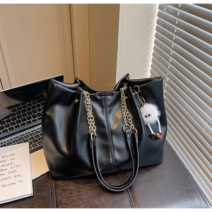 Detail of a black leather tote bag with gold chain and plush monster charm on desk