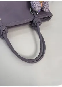 Detail of purple faux leather bucket bag showing twisted handle and bow charm
