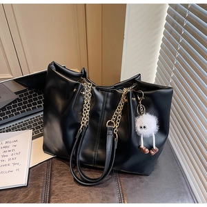 Detail of black tote bag with gold chain handle and plush charm in office setting