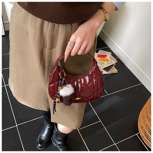 Close-up of quilted burgundy leather crescent bag with white fur ball and golden bell charm
