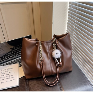 Detail of a brown tote bag featuring golden chain straps and a plush white eye charm