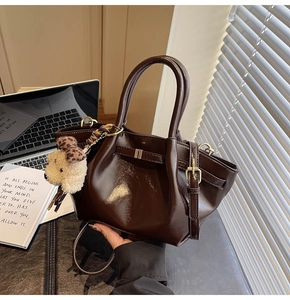 Détail d'un sac cabas en cuir verni marron foncé avec pendentif ours en peluche et nœud