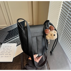 Detail of black litchi grain leather shoulder bag with a cute plush bear charm