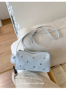 Détails du sac tonneau bleu clair avec clous étoiles argentés et pendentif cœur sur canapé