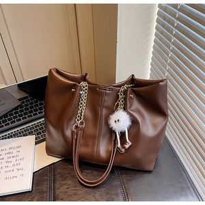 Close-up of dark brown leather tote bag with gold chain strap and plush monster charm